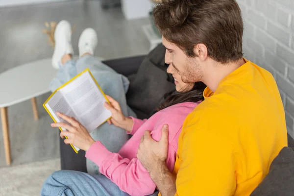 Glückliches junges Paar umarmt und liest Buch im Wohnzimmer — Stockfoto