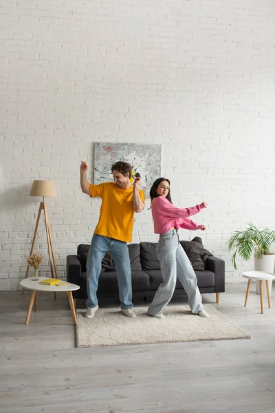 Positives junges Paar in lässiger Kleidung tanzt im Wohnzimmer — Stockfoto