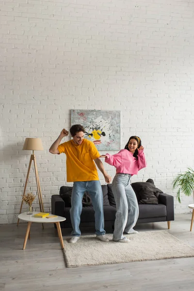 Pareja joven positiva en ropa casual bailando juntos en la sala de estar - foto de stock