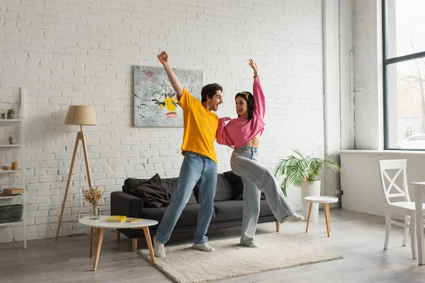 Sourire jeune couple en vêtements décontractés dansant dans le salon — Photo de stock