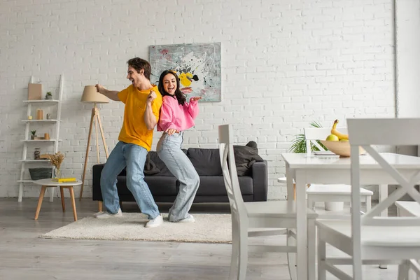 Sonriente pareja joven en ropa casual bailando en la sala de estar moderna - foto de stock