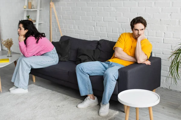 Disappointed young man with hand near face sitting on couch near girlfriend in living room — Stock Photo