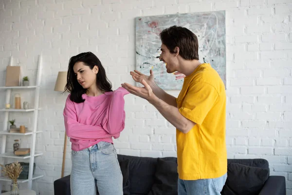 Angry young man yelling with outstretched hands near girlfriend in living room — Stock Photo