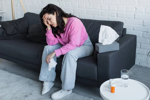 Kranke junge Frau sitzt auf Couch, die Hand vor dem Gesicht und hält Papierserviette im Wohnzimmer — Stockfoto