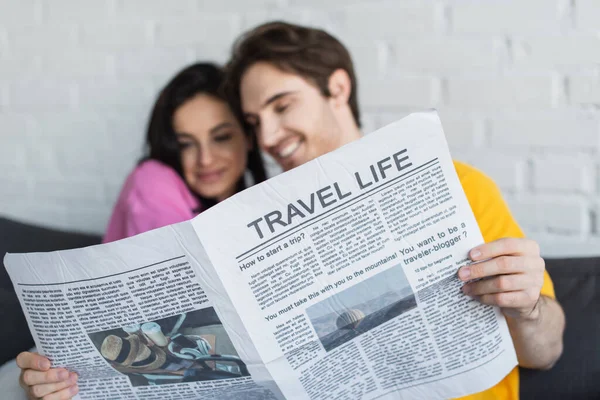 Smiling young couple sitting on couch, hugging and holding newspaper at home — Stock Photo