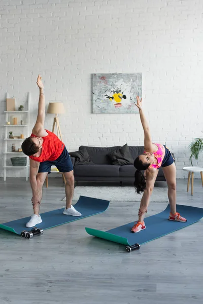 En forma pareja joven en ropa deportiva haciendo ejercicio en colchonetas de fitness en casa - foto de stock