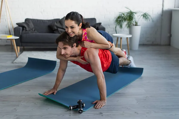 Smiling fit young woman lying on back of man doing plank at home — Stock Photo