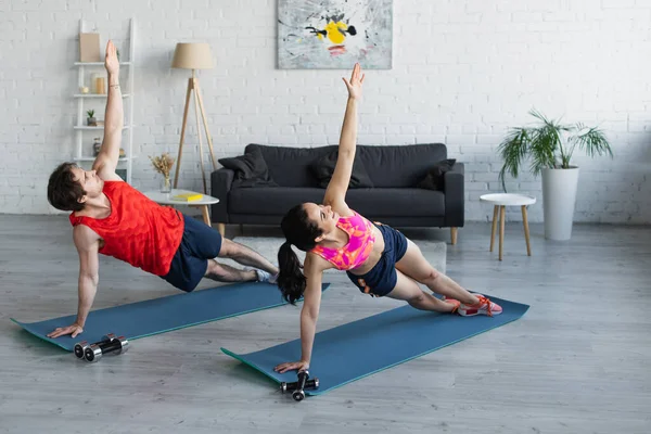 Atlético jovem casal no sportswear fazendo exercício em tapetes de fitness em casa — Fotografia de Stock