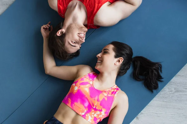 Draufsicht auf lächelndes junges Paar in Sportbekleidung, das auf Fitnessmatten liegt und sich zu Hause anschaut — Stockfoto