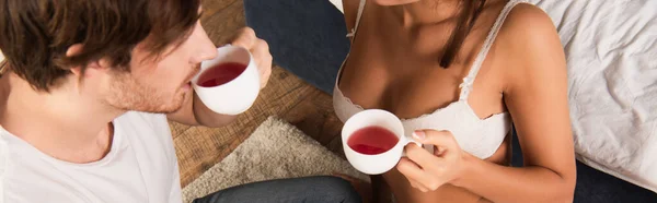 Обрезанный вид женщины в сексуальном лифчике, пьющей чай с парнем, баннер — стоковое фото