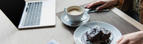 Vue recadrée de la femme assise près du café, du dessert et de l'ordinateur portable avec écran blanc dans le café, bannière — Photo de stock