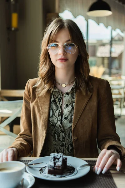 Stilvolle Frau blickt bei Kaffee und Dessert im Café in die Kamera — Stockfoto