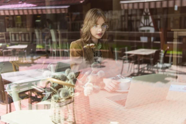 Libero professionista con caffè e computer portatile seduto vicino alla finestra in caffè — Foto stock