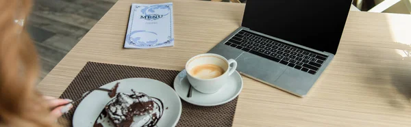 Vista ritagliata del computer portatile con schermo bianco, caffè e menu vicino alla donna con dessert in primo piano sfocato in caffè, banner — Foto stock