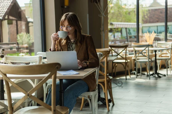 Trendy freelancer printing coffee at using laptop in cafe — стоковое фото