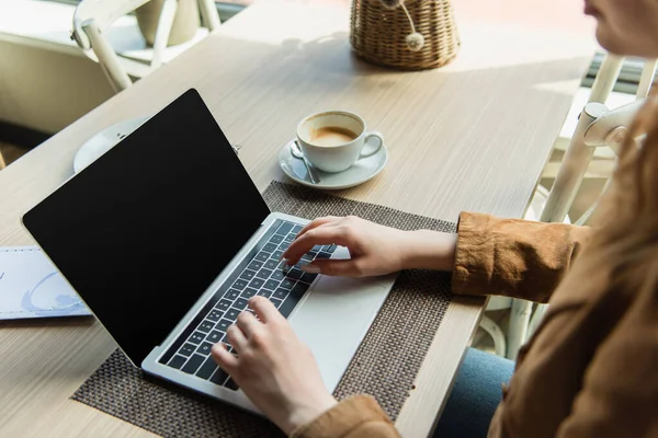 Vista cortada da mulher usando laptop com tela em branco perto de café no café — Fotografia de Stock