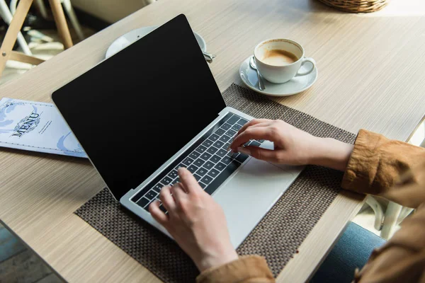 Vista cortada do blogueiro usando laptop perto do menu e xícara de café no café — Fotografia de Stock