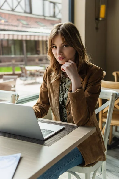 Elegante freelance guardando macchina fotografica vicino a computer portatile in caffè — Foto stock