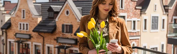 Femme élégante avec smartphone tenant des tulipes à l'extérieur, bannière — Photo de stock