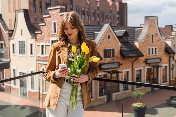 Donna sorridente con smartphone che tiene tulipani all'aperto — Foto stock