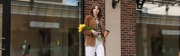 Стильна жінка з паперовою чашкою тримає тюльпани і ходить на відкритому повітрі, банер — стокове фото