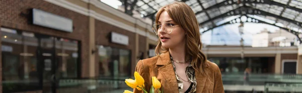 Молода жінка в сонцезахисних окулярах тримає жовті тюльпани, банер — стокове фото
