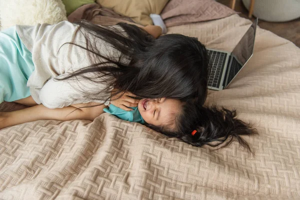 Madre baci allegro asiatico figlia vicino offuscata laptop su letto — Foto stock