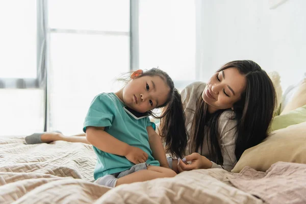 Азійська дитина розмовляє на смартфоні поруч із мамою на ліжку. — стокове фото