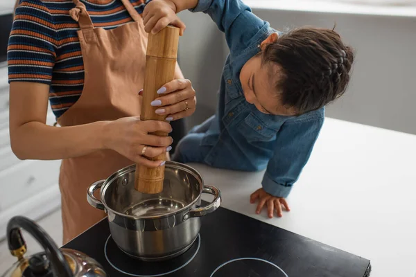 Asiatique enfant tenant moulin à sel tandis que la mère cuisine dans la cuisine — Photo de stock