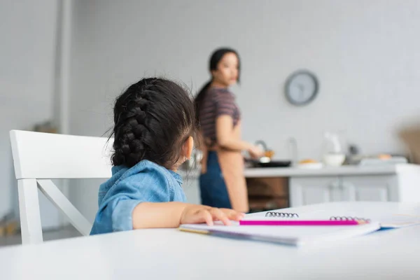 Niño sentado cerca de lápiz y papel en la cocina - foto de stock