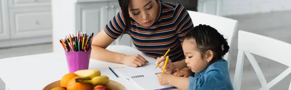 Asian mother and kid drawing near fruits in kitchen, banner — Stock Photo