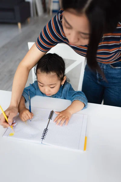 Asian toddler kid drawing on notebook near blurred mother — Stock Photo