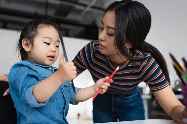 Asiatische Mutter schaut Tochter mit Buntstiften an — Stockfoto