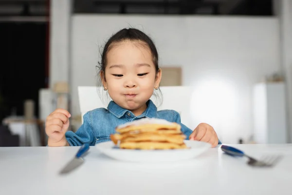 Asian kid sitting near blurred pancakes on table — Stock Photo