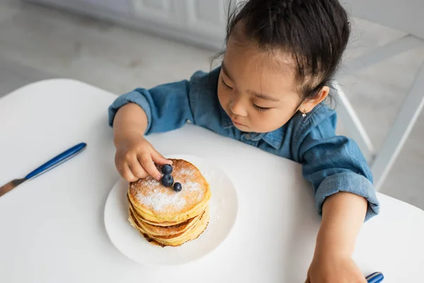 Vue grand angle de l'enfant asiatique prenant myrtille de crêpes à la maison — Photo de stock