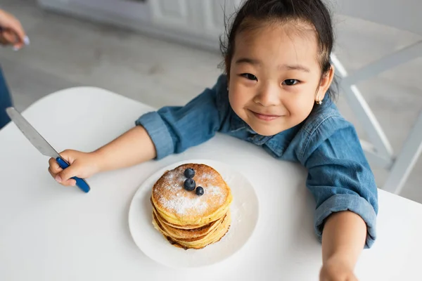 Vue grand angle de positif asiatique enfant regardant caméra près de savoureux crêpes — Photo de stock