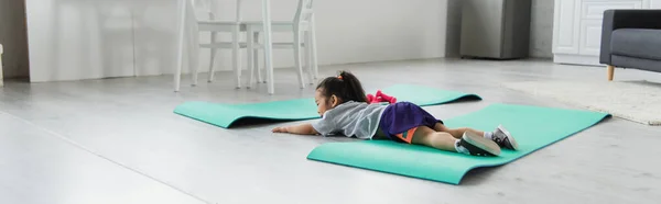 Маленькая азиатка в спортивной одежде лежит на коврике дома, баннер — стоковое фото