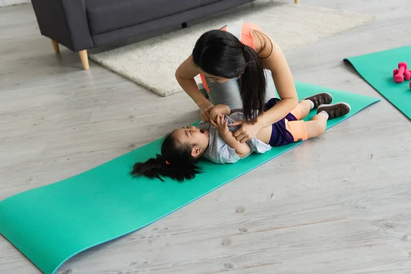 Mother tickling cheerful asian kid on fitness mat — Stock Photo