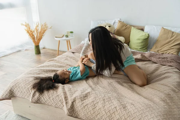 Madre solletico asiatico figlia su letto — Foto stock