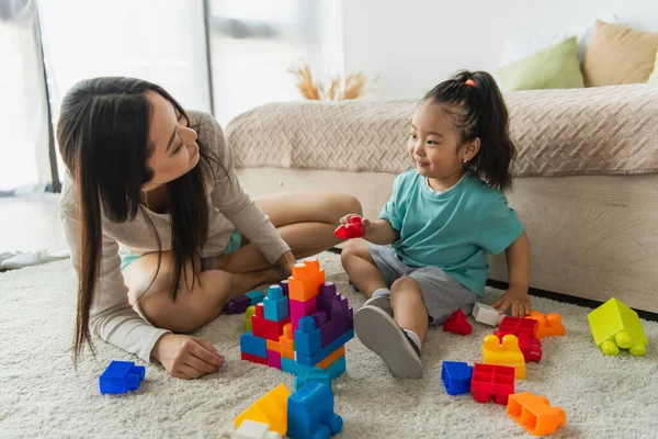 Asian parent sitting near daughter and building blocks at home — Stock Photo