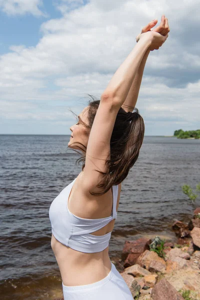 Brunette and young woman with closed eyes and raised hands near sea — Stock Photo