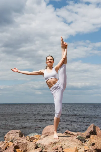 Cheerful woman in sportswear standing hand to big toe pose near sea — Stock Photo