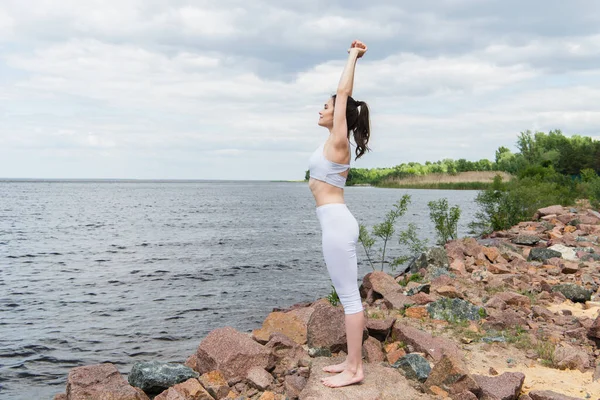 Volle Länge der jungen Frau in Sportbekleidung praktiziert Yoga in der Nähe des Meeres — Stockfoto