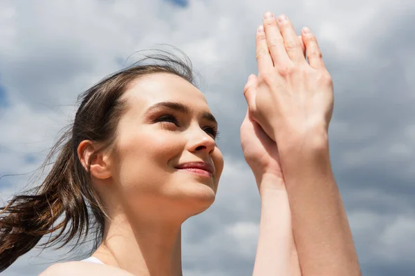 Низкий угол зрения счастливой женщины с сжатыми руками против голубого неба с облаками — стоковое фото