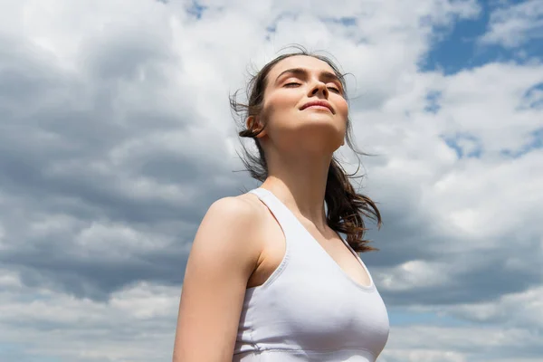 Low angle view of young woman with closed eyes against blue sky with clouds — Stock Photo