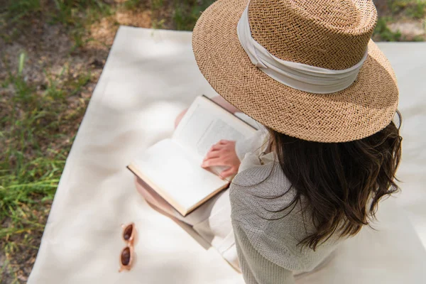 Overhead view of young woman in straw hat reading book in forest — Stock Photo