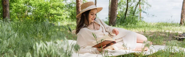 Fröhliche junge Frau mit Strohhut liest Buch im Wald, Banner — Stockfoto