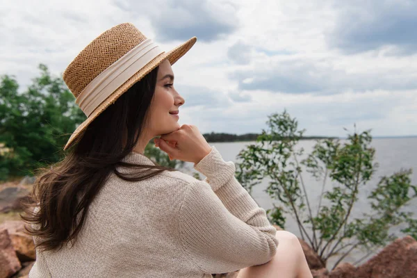 Feliz jovem mulher em chapéu de palha sentado perto do mar — Fotografia de Stock
