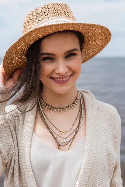 Happy young woman adjusting sun hat and looking at camera — Stock Photo