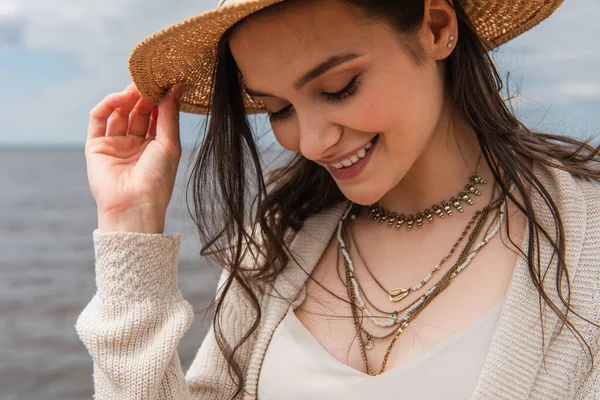 Mujer joven positiva ajustando sombrero de sol fuera - foto de stock